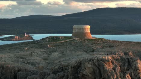 Golden-hour-glow-on-defence-tower-in-Fornells-Bay,-Menorca-Spain