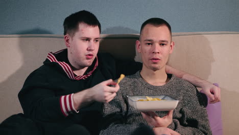 two friends enjoying chips and watching tv