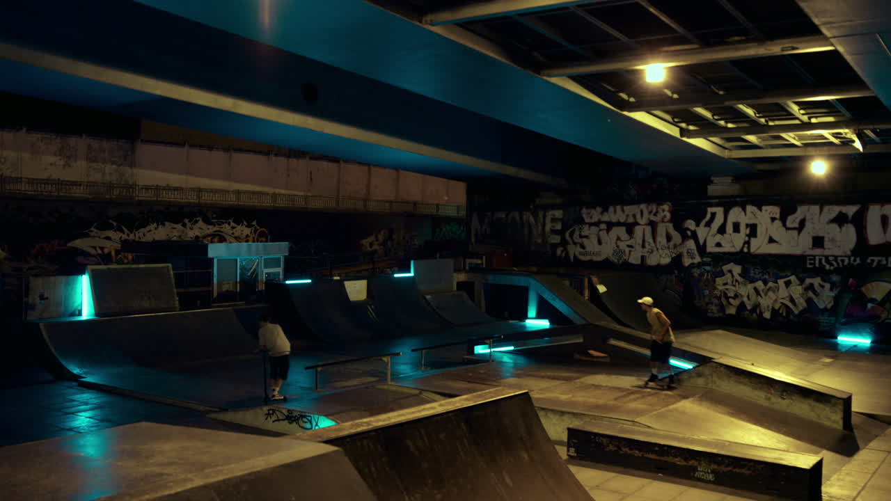 Hipster attivi in giro insieme in skatepark notturno con muro graffitato.