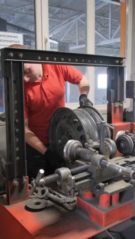 man repairing a car wheel rim on specialized machinery in a workshop