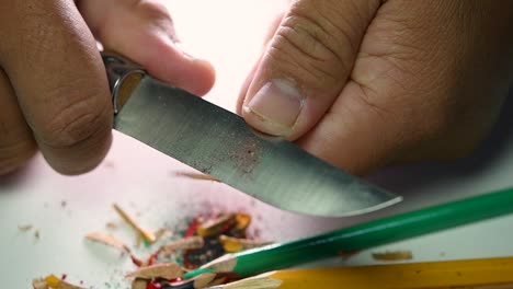 footage of hands slowly sharpening a pencil and some coloured pencils with a sharp knife