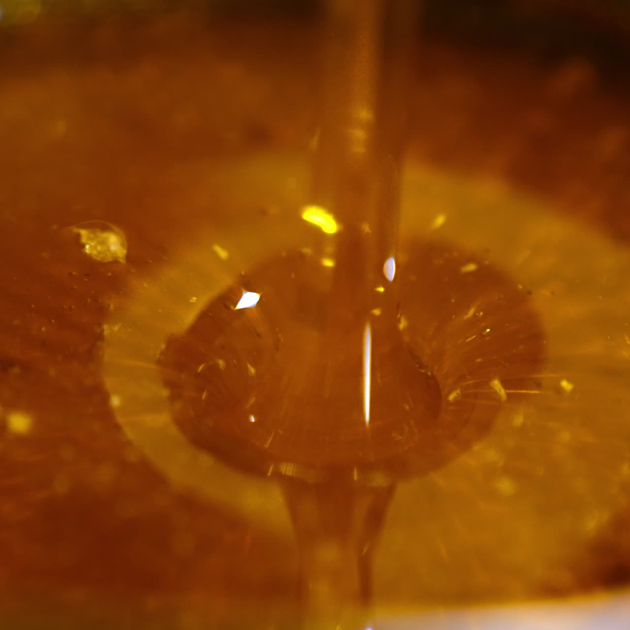 Amber honey flowing into the dish. Beautiful fresh organic product being poured onto the metal sieve for cleansing