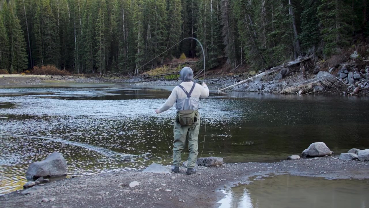 Still wide-angle ground shot of a solo fisherman casting at a quiet alpine lake on Colorado's Grand Mesa, fishing for rainbow and brook trout in the Rocky Mountains.
