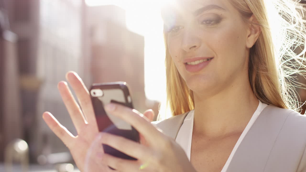 Bella donna bionda che usa lo smartphone, con un bagliore di luce solare.