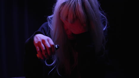 Depressed-blonde-woman-hiding-face-stressfully-smoking-disposable-vape-while-sitting-in-a-dark-room