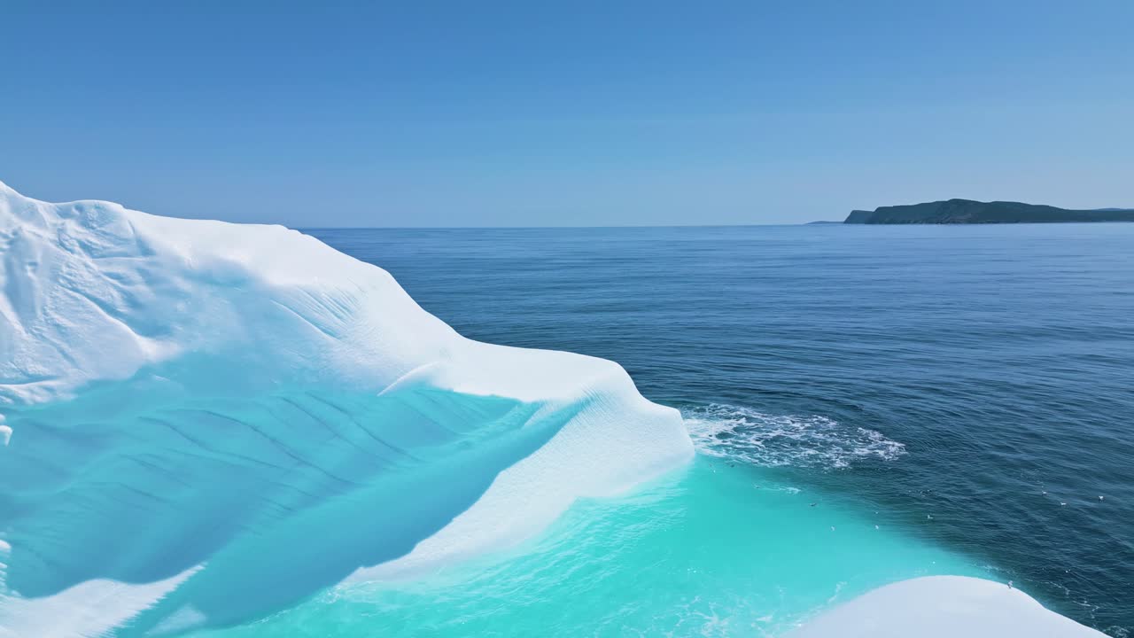 Aerial footage of a large iceberg off Flatrock, Newfoundland, featuring vivid turquoise meltwater in calm Atlantic waters.