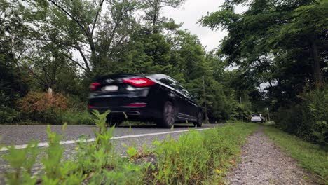 Van-and-other-cars-drive-through-forested-landscape,-low-angle-static-view-looking-up-at-vehicles