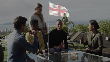 friends on rooftop with england flag, drinking and snacking, celebrating together