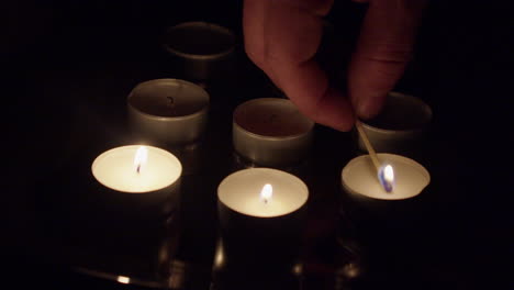 Los-Dedos-Sostienen-Una-Cerilla-De-Madera-Encendida-Para-Encender-Velas-De-Té-En-Una-Habitación-Oscura.