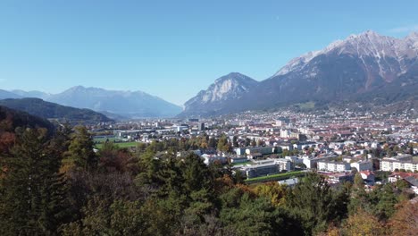 Aerial-view-of-the-city-of-Innsbruck-from-the-hills-of-a-forest-on-a-sunny-autumn-day-and-a-blue-sky-and-in-the-background-the-alps-with-their-peaks,Tyrol,-Austria,-Europe