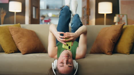 auriculares chica acostando sofá escuchando música de cerca. mujer feliz enviando mensajes de texto al teléfono