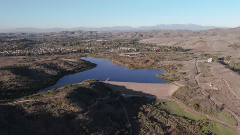 Sweeping-Shot-of-Lake-with-Dam-Surrounded-by-Hiking-Trails-and-Suburbs