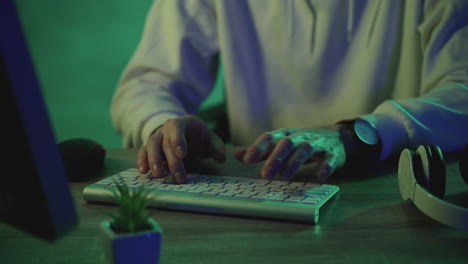 male hands typing on the keyboard working with a computer on a green colorful background. close-up.