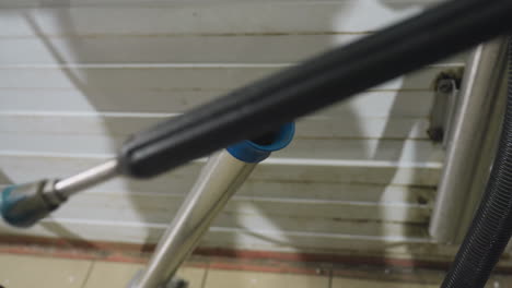 close up of hand removing high pressure car wash hose from wall-mounted holder with reflection of person visible on wooden panel wall inside garage during preparation for vehicle cleaning service