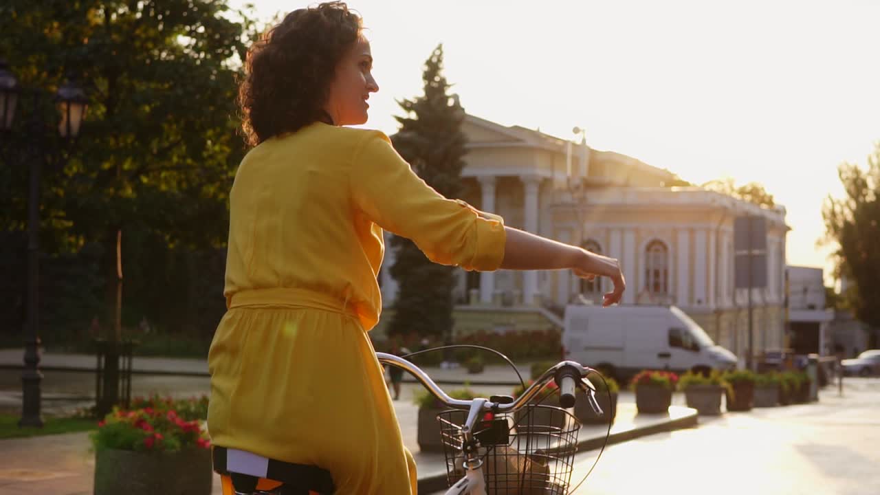 Back view of a beautiful woman riding a citibike with a basket and flowers in the city center showing her thumb up. Lens flare