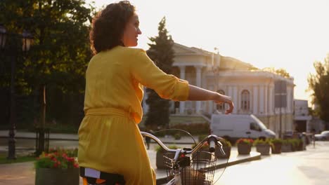 back view of a beautiful woman riding a citibike with a basket and flowers in the city center showing her thumb up. lens flare