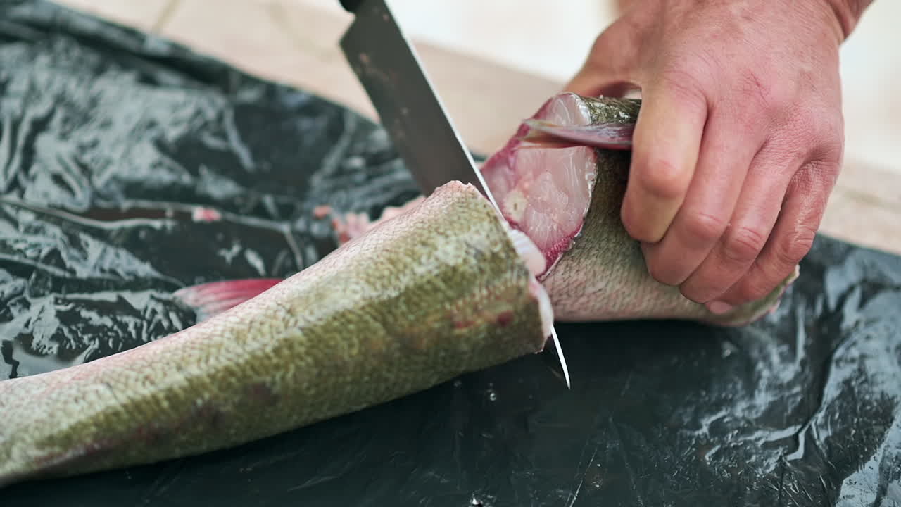 Close up of hands cutting a fish tail on a black surface with a knife
