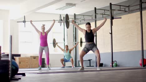 concentradas en un grupo de mujeres diversas entrenando en el gimnasio juntas levantando barras, en cámara lenta