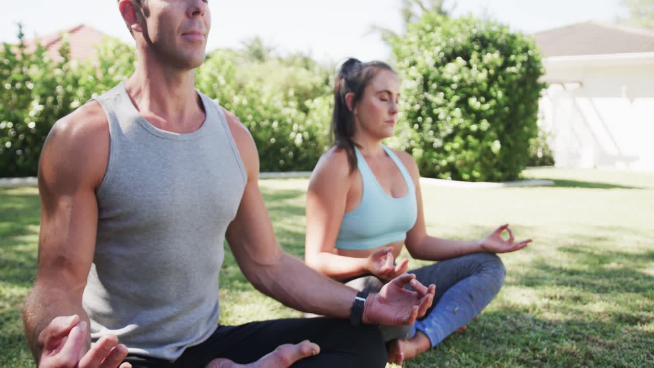 feliz pareja caucásica practicando meditación de yoga en un jardín soleado, cámara lenta