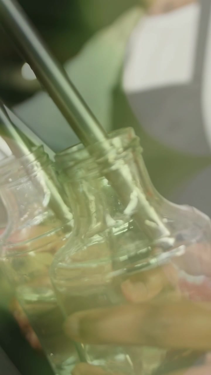 Vertical video: Beverage server bringing bottle inserting steel nozzle filling glass bottles evenly