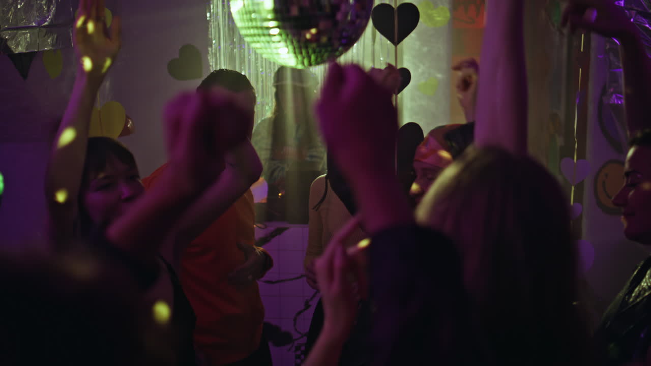 Gruppo di frequentatori di discoteche che alzano le mani verso la palla da discoteca, divertendosi in una discoteca vivace.