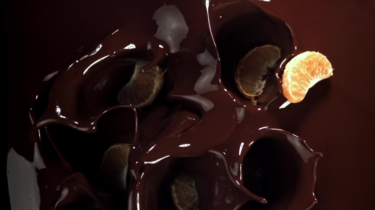 Gajos de mandarina pelados salpicando en chocolate fundido intenso