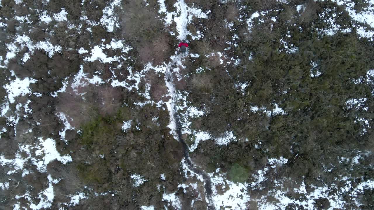 A 4K overhead drone shot of a man walking along a frozen wilderness path.