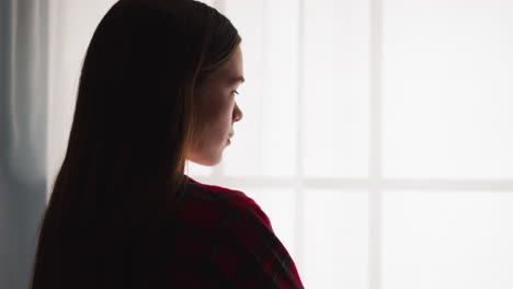 Elegant-young-woman-stands-near-window-in-room-backside-view