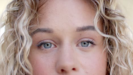 Retrato-De-Cerca-De-Ojos-Azules-De-Una-Mujer-Caucásica-Con-Cabello-Rubio-Rizado-Sonriendo,-Cámara-Lenta