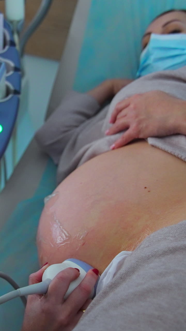 Medical specialist performing ultrasound check for pregnant lady. Patient lies on her side while doctor moves the device by her belly. Vertical video