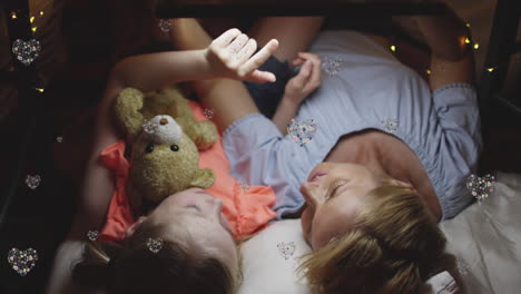 animación de corazones sobre madre y hija caucásicas acostadas en la cama