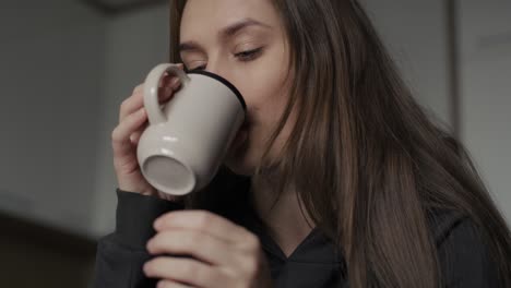 mujer caucásica triste sentada en el sofá con una taza de café.