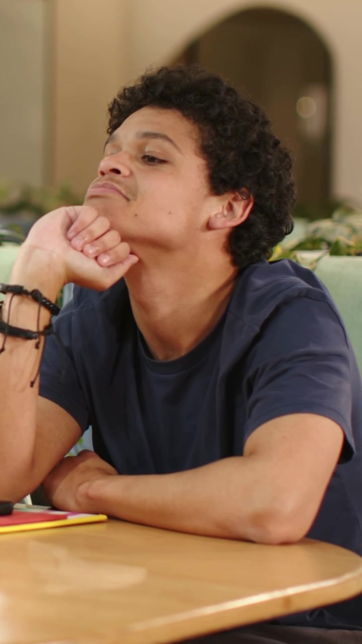 Vertical video: Resting chin on fist, man wearing navy tee tilting head at home table, notebook