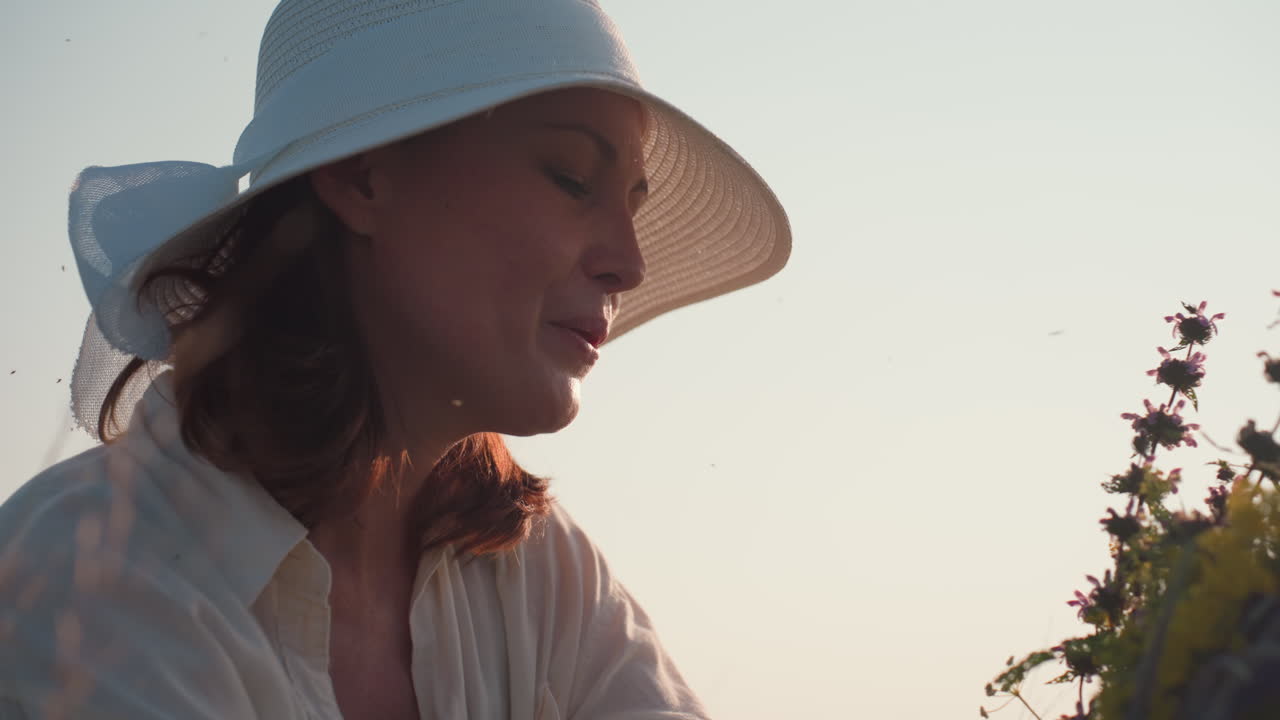 woman gently holds wildflower bouquet close to face while enjoying scent during golden hour, peaceful moment in soft sunlight with tiny insects flying around