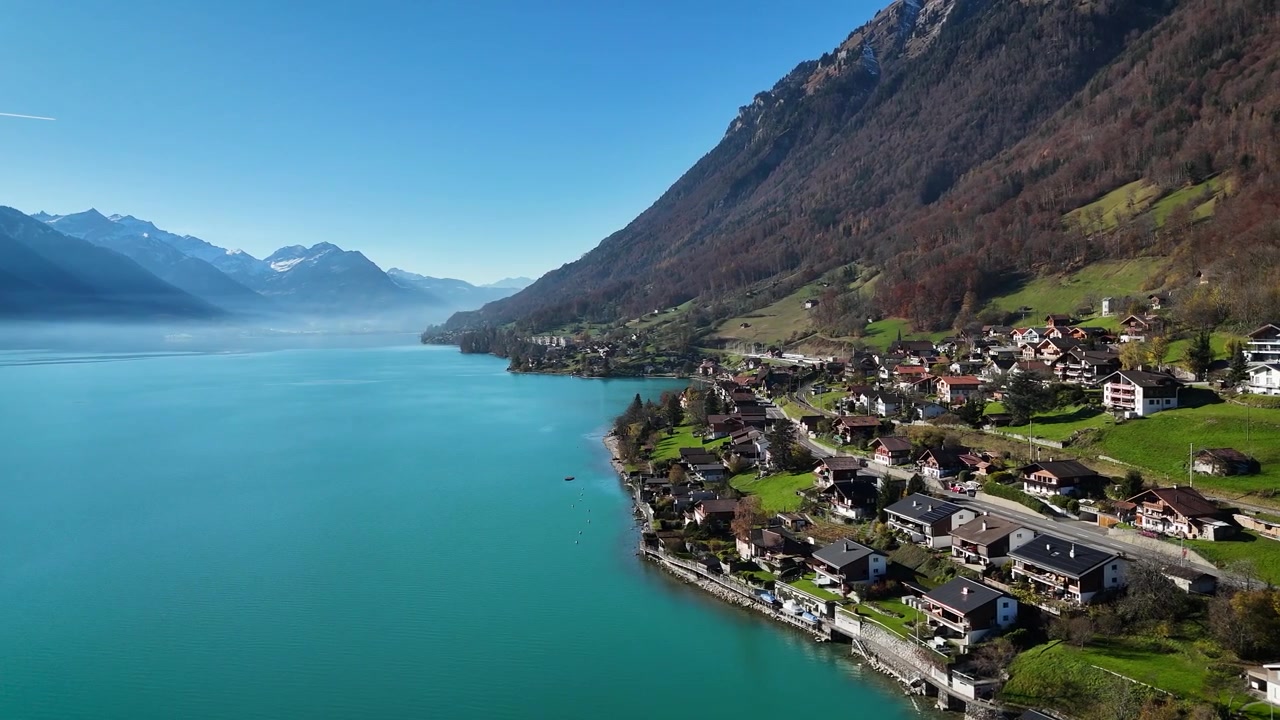 Ripresa aerea con drone sopra il Lago di Brienz all'alba, con acque blu mozzafiato, il villaggio di Sigriswil e le Alpi sullo sfondo