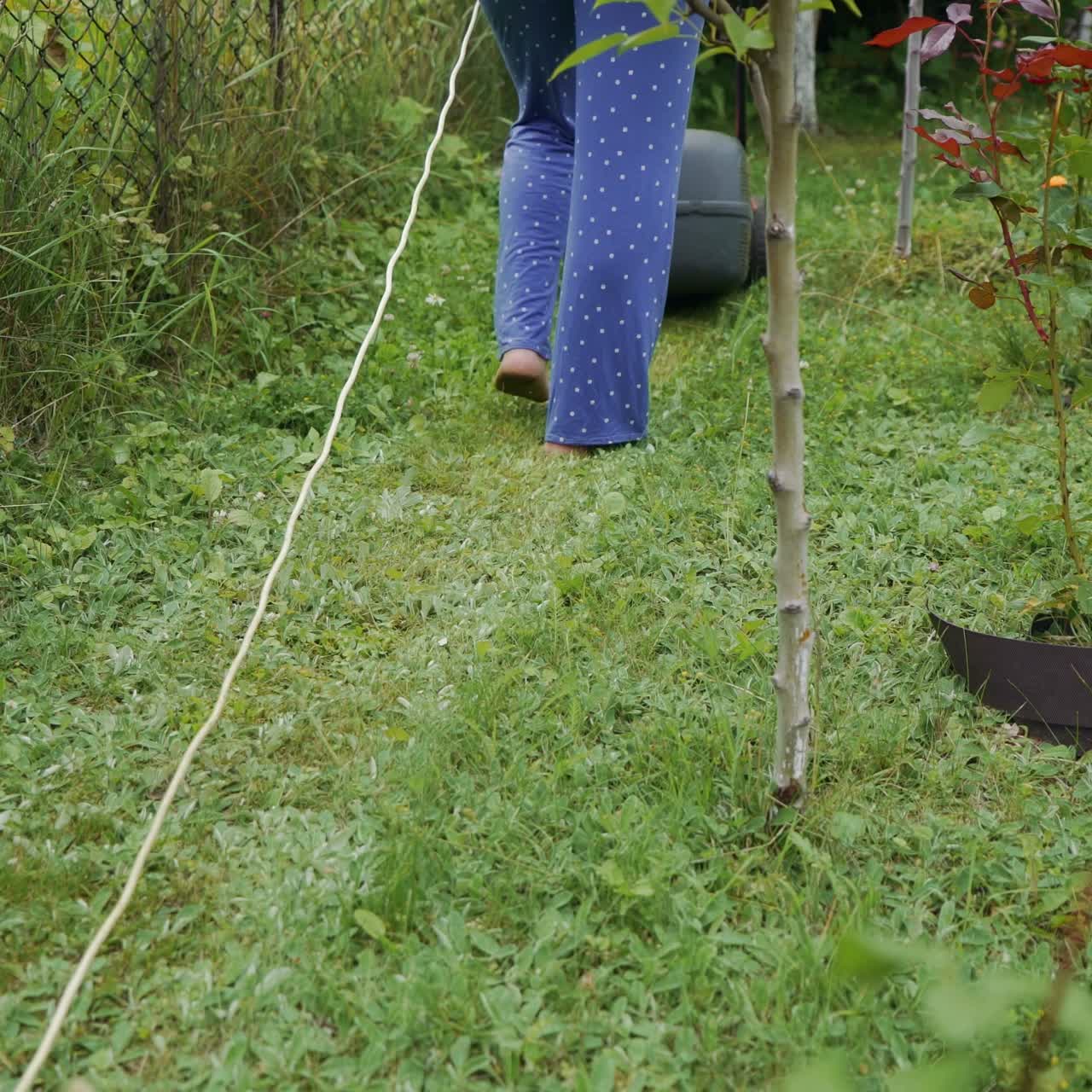 Legs of young woman mowing lawn by lawn mower near country house