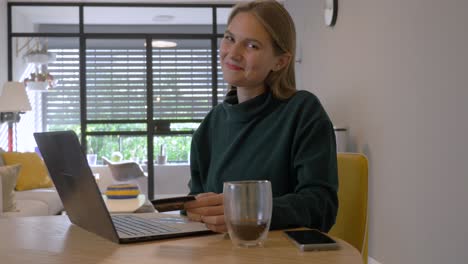 Pretty-Women-buying-Online-through-laptop-Using-Her-Credit-card-and-Smiling-to-the-Camera