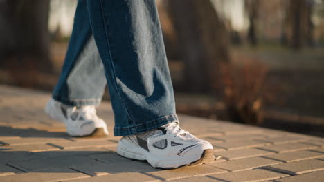 a close-up view of a person wearing jeans and white shoes, walking slowly on a paved path in a park. calm and deliberate pace of the steps, conveying a sense of sadness and introspection