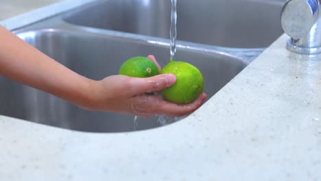 hands washing limes under running water in a kitchen sink, highlighting cleanliness and freshness in a domestic setting