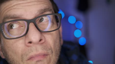 a man with glasses looking at the camera and all around, then smiling, with a blue, defocused background