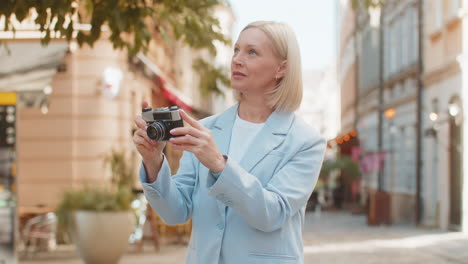 happy mature businesswoman using vintage camera to take photos of fascinating city on street