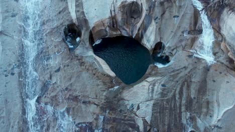 aerial top view shot descending on cascading waterfalls and deep pools of water in granite rock