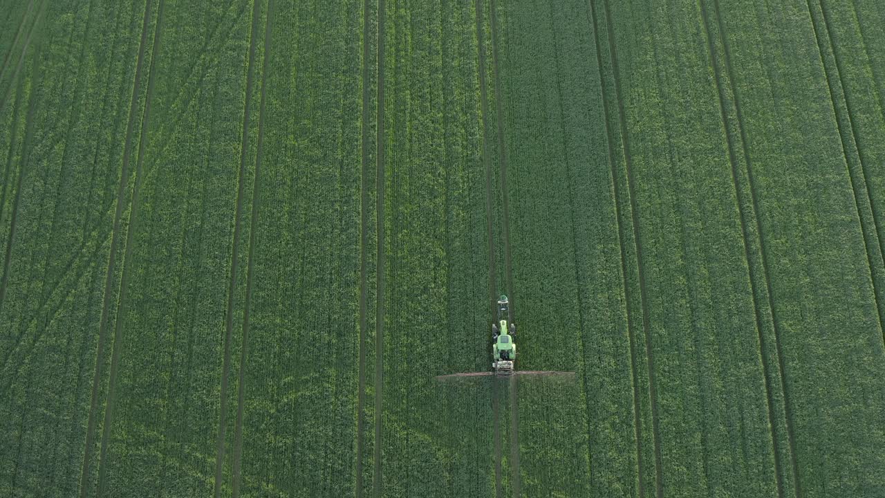 antena vertical de un campo de cultivo verde intenso que está siendo rociado por un tractor