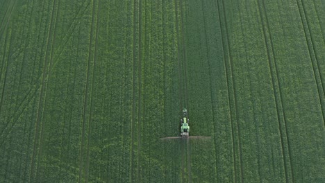 vertical aerial of vivid green crop field being sprayed by tractor