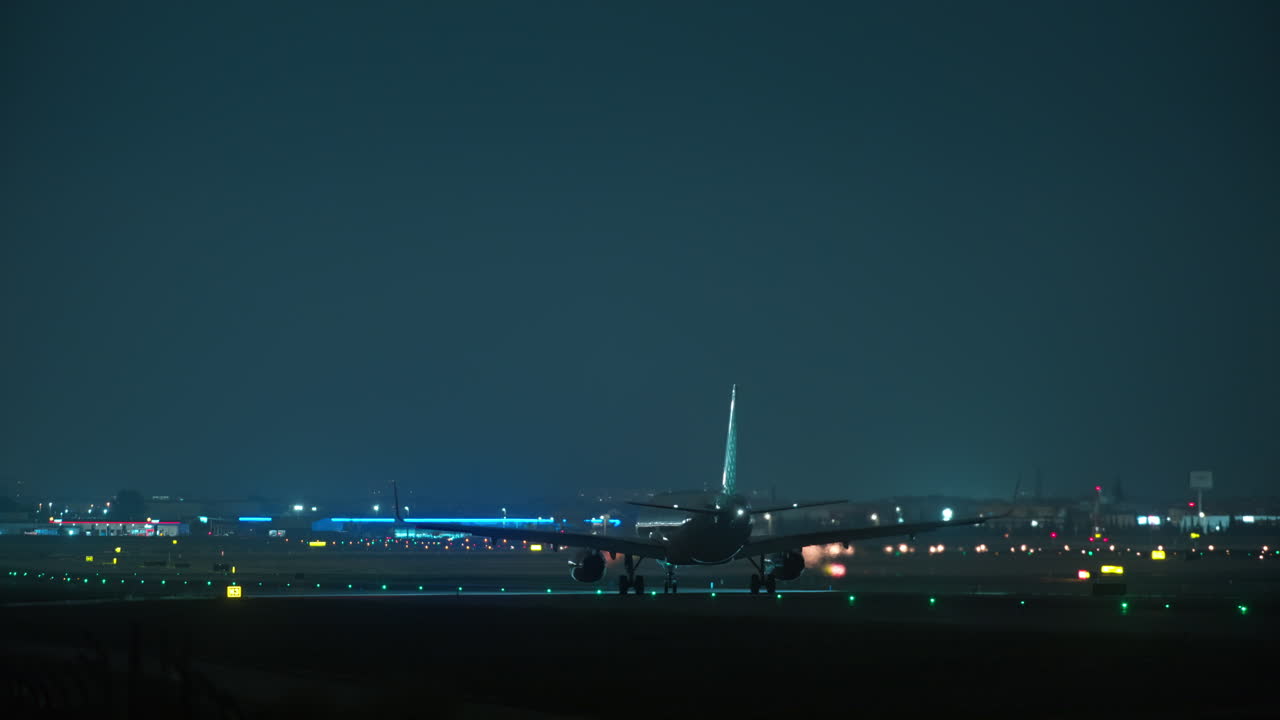 夜間、空港の灯火が輝く滑走路をタキシングする飛行機