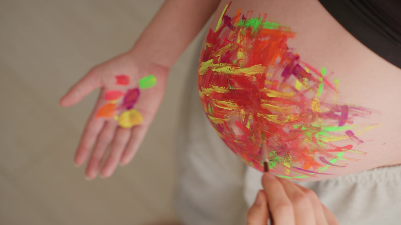 Primo piano di una donna incinta che dipinge il suo pancione con colori vivaci