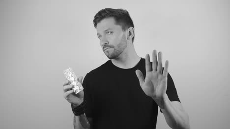 slow motion footage of a tattooed man holding up white painkillers with his hand and the other one indicating not to take them