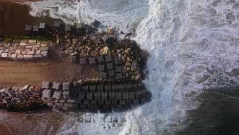 Aerial-top-down-shot-of-waves-of-rocky-coast-and-sandy-beach-at-sunset-time