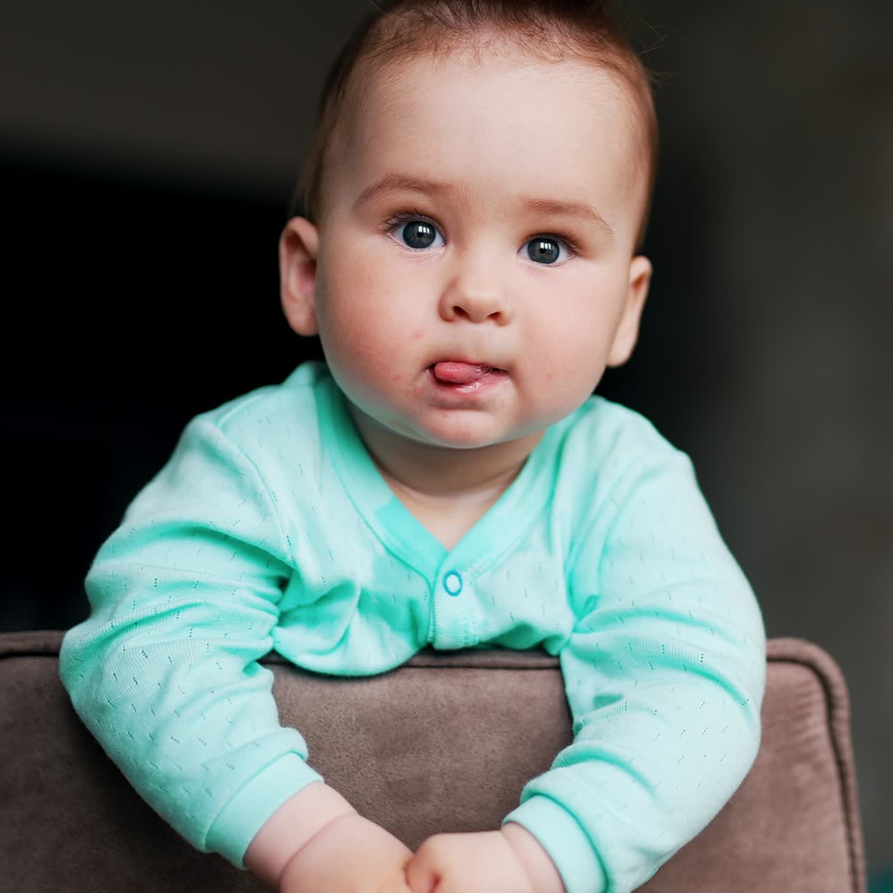 Serious interested kid standing on the chair looks around. Curious baby studying surrounding leaning on a chair back. Low angle view