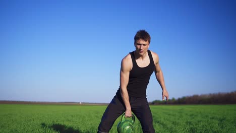 Handsome-young-athlete-in-dark-clothes,-throws-weight-from-hand-to-hand.-The-weight-is-scrolled-to-the-air.-Outdoors.-Slow